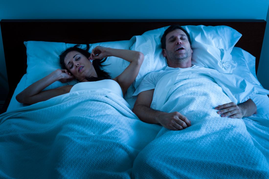 Man snoring in bed while woman is annoyed