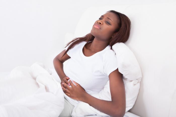 A woman is lying in bed with a painful stomach.