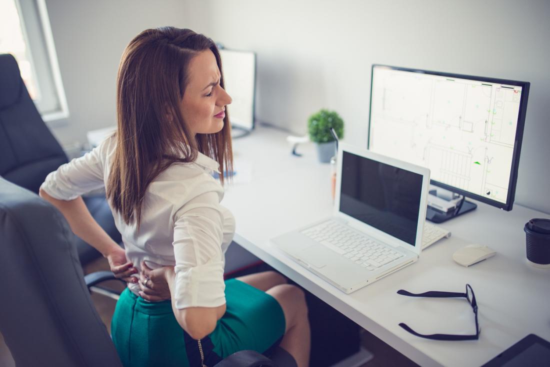 Woman with lower back pain sitting at desk.