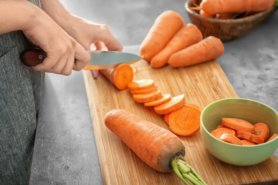 Person cutting up carrots containing beta carotene on chopping board