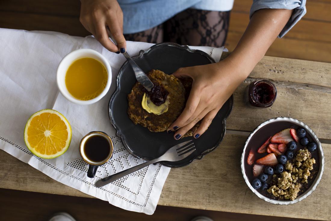 Person preparing healthy breakfast with fruit, cereal, tea, whole grain, and spread.