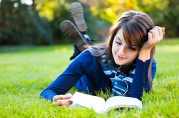 College student reading, lying outside on grass