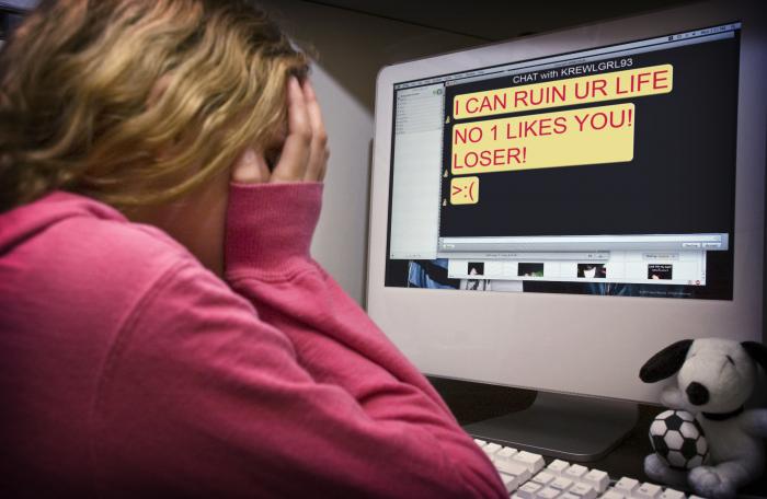 A child in front of a computer with cyberbullying language on the screen.