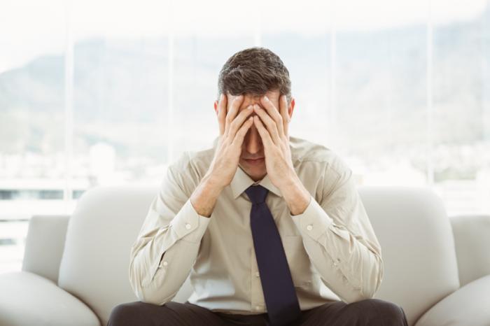 A stressed man on a sofa holds his head in his hands.