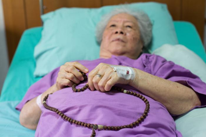 A hospital patient holds onto some prayer beads in bed.