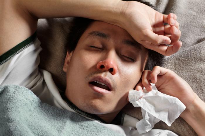 An ill man is lying down with a tissue.
