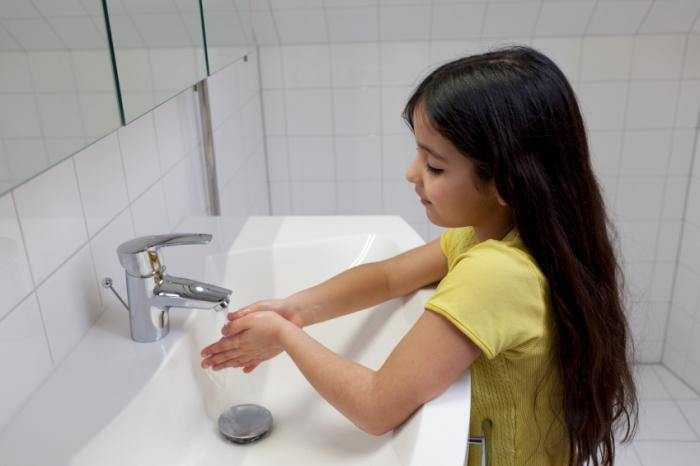 A girl is running her hands under a tap.