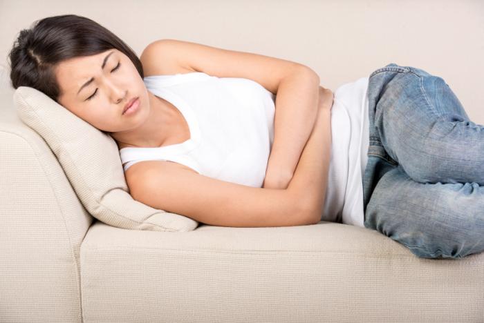 Woman on a sofa holding her abdomen in discomfort.