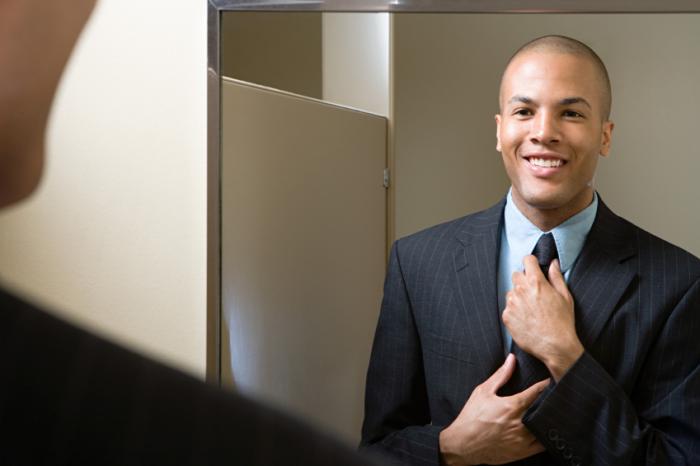 A man adjusting tie smiling in mirror