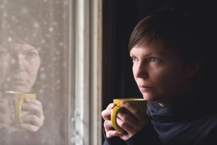 woman staring through window holding cup