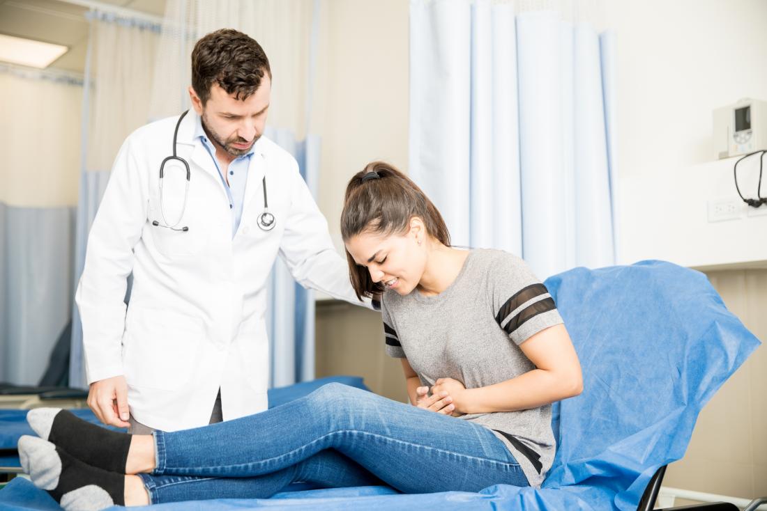 Woman holding stomach in pain on łóżko szpitalne with doctor by side.