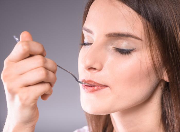 A woman with closes eyes eats some food from a metal spoon
