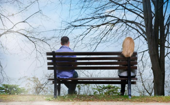 A man and woman sit at opposite ends of a bench
