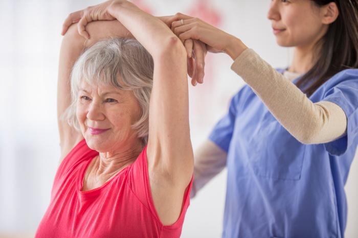 Older lady being helped with some light fitness