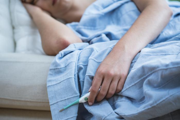 person in bed with the flu holding a thermometer