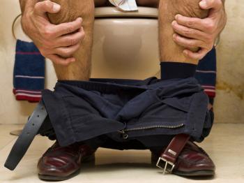 [Man sits on toilet with clenched hands]