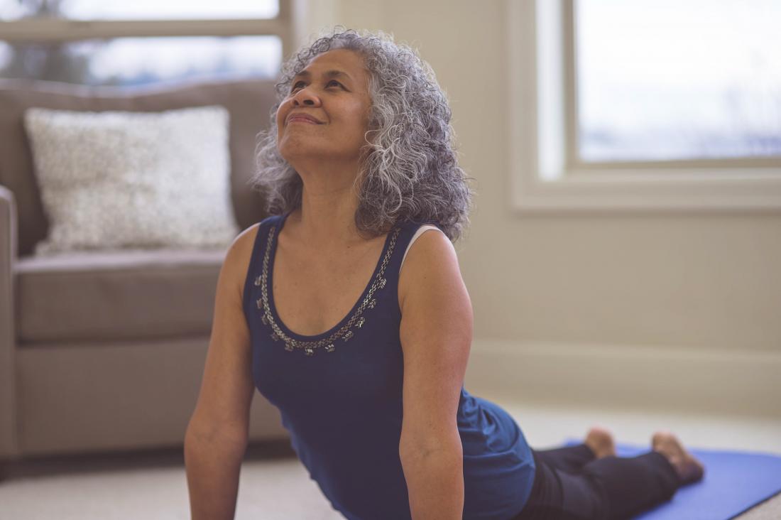 older woman lifts her torso off the ground in a yoga pose at home