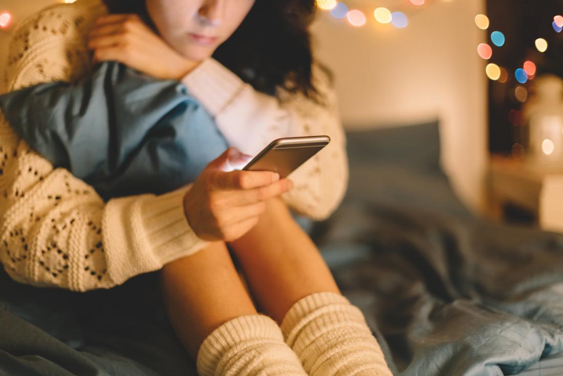 woman checking smart phone on her bed