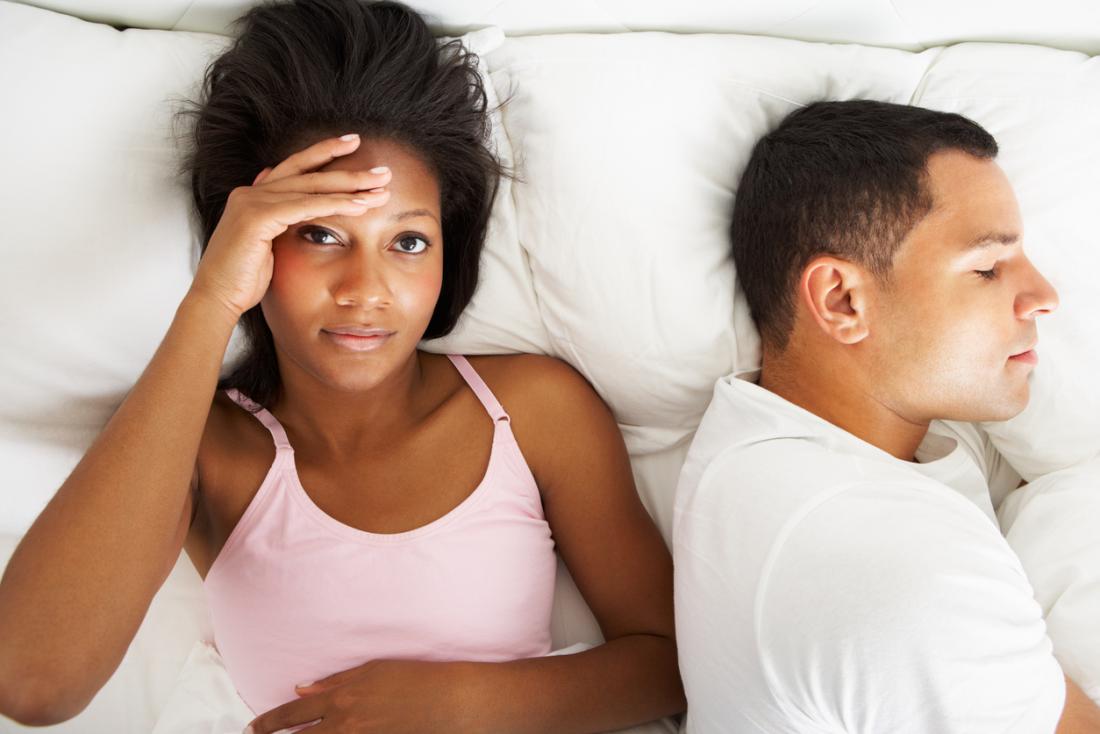 woman looking annoyed in bed next to sleeping man