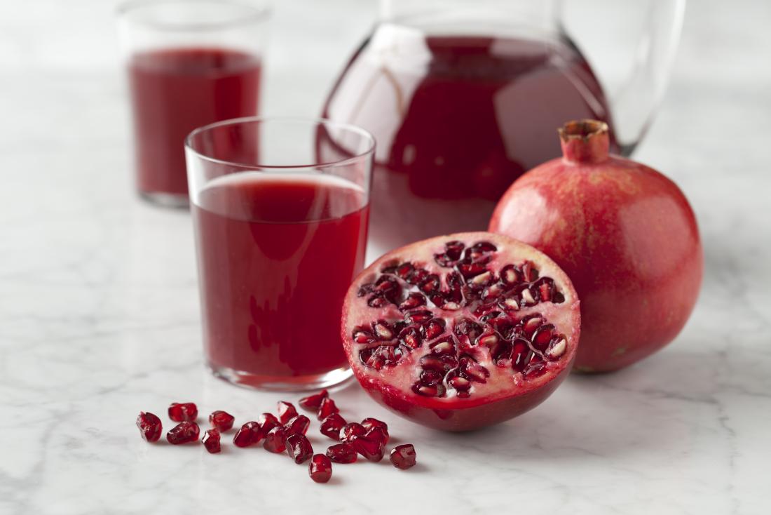 Halves pomegranate with seeds and pomegranate juice on marbled surface.