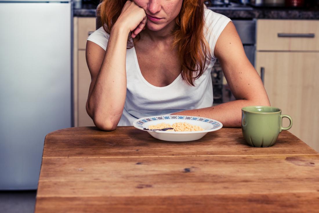 Sad woman alone in front of bowl of cereal.