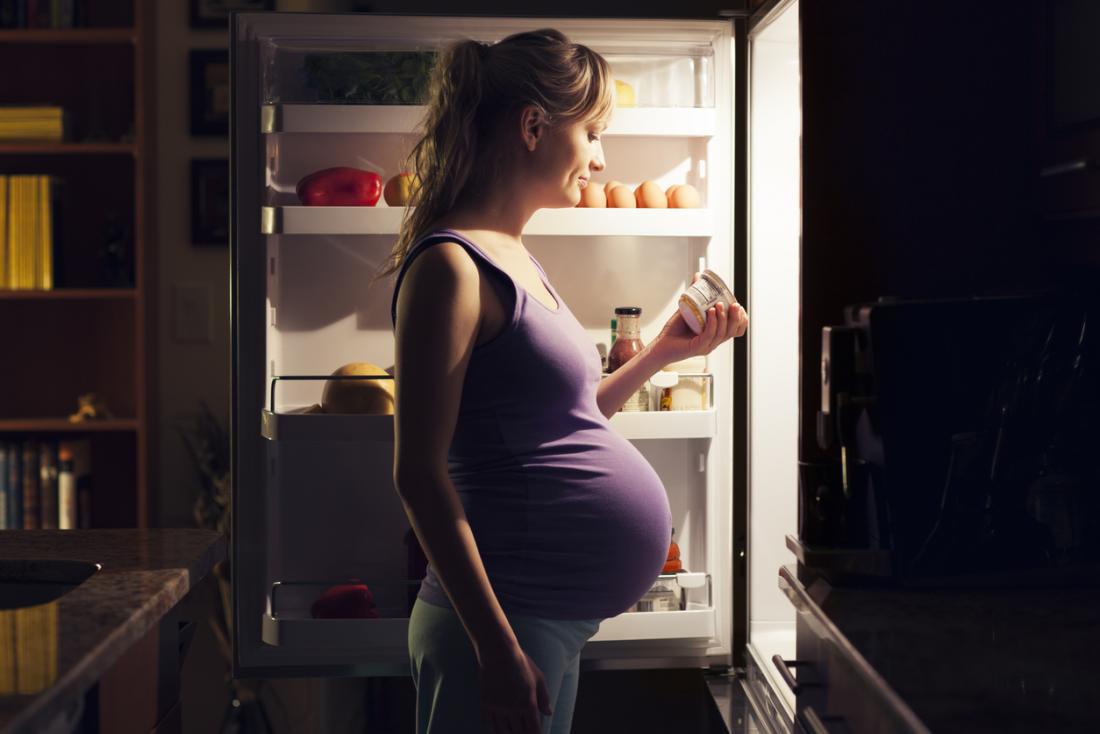 Pregnant woman looking into fridge at night.