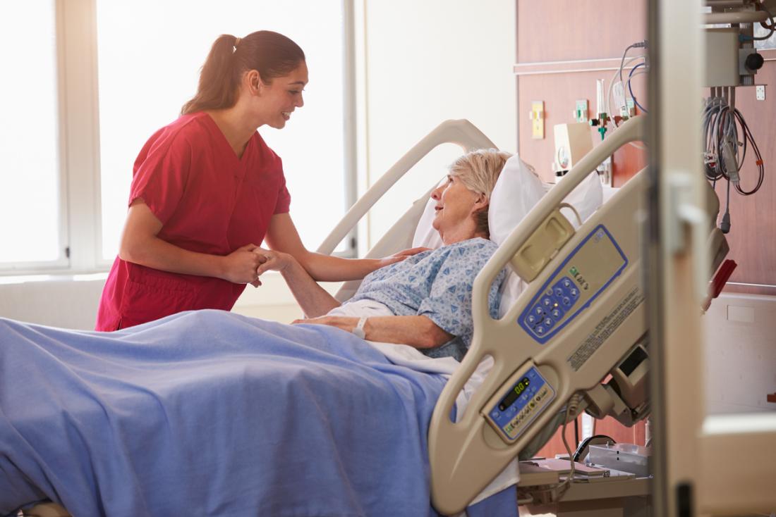Older female patient in hospital bed with nurse.