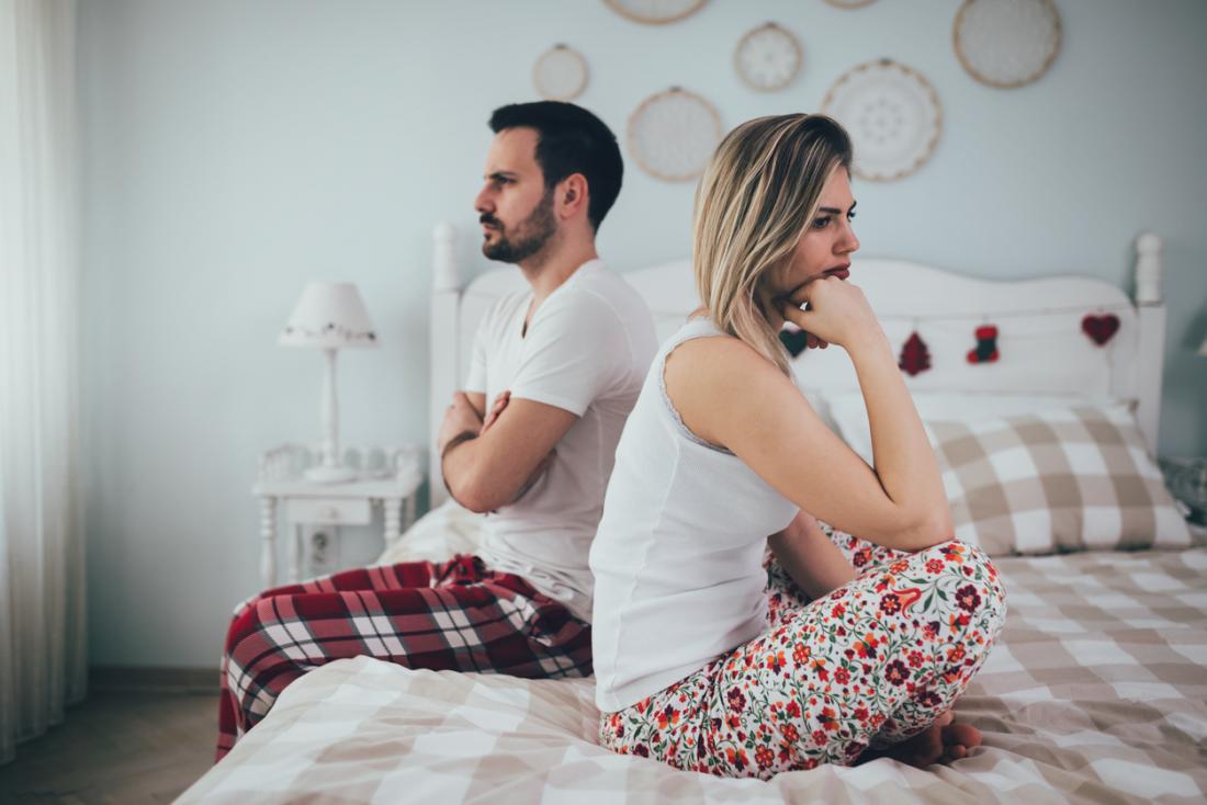 a couple sitting on the bed ignoring each other