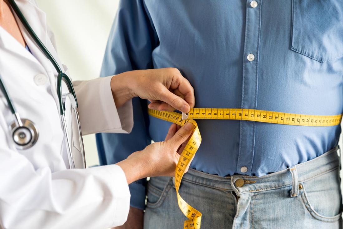 Obese man having waist measured by doctor.