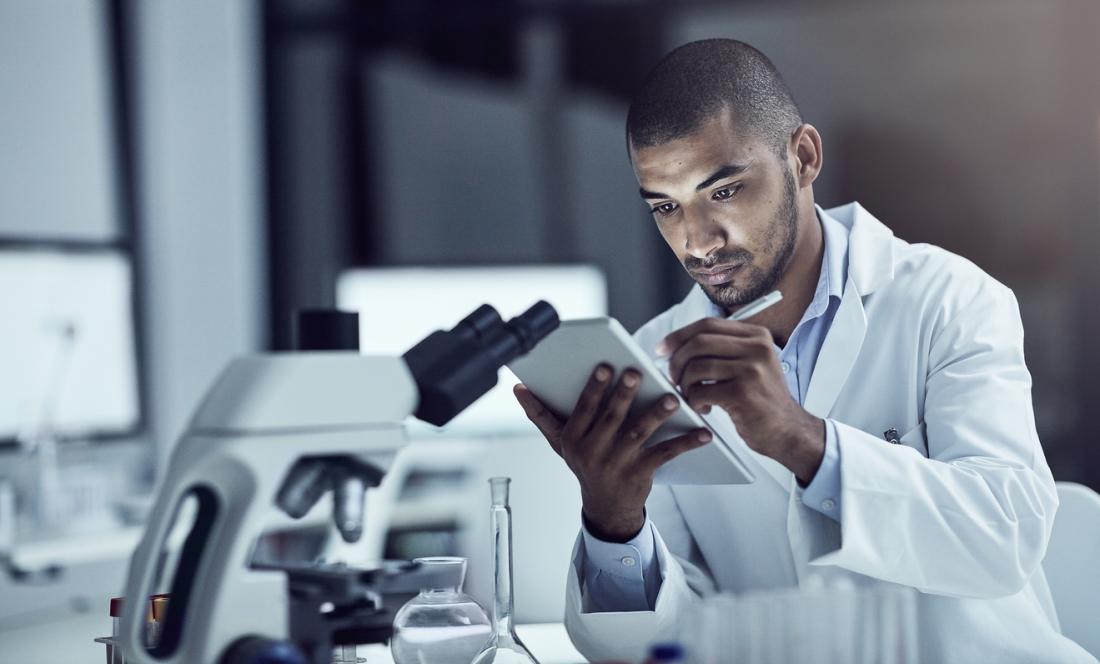 Lab tech writing notes in front of microscope.