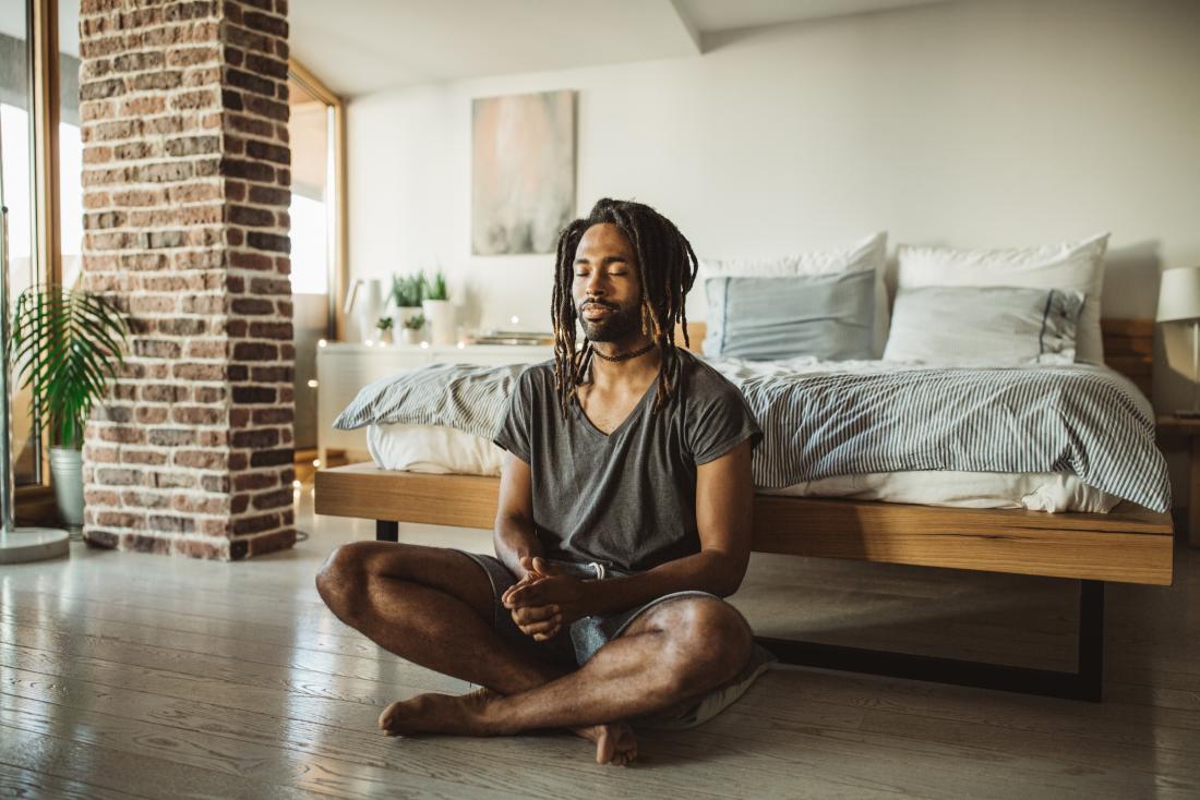 Man practicing mindful meditation and yoga in bedroom
