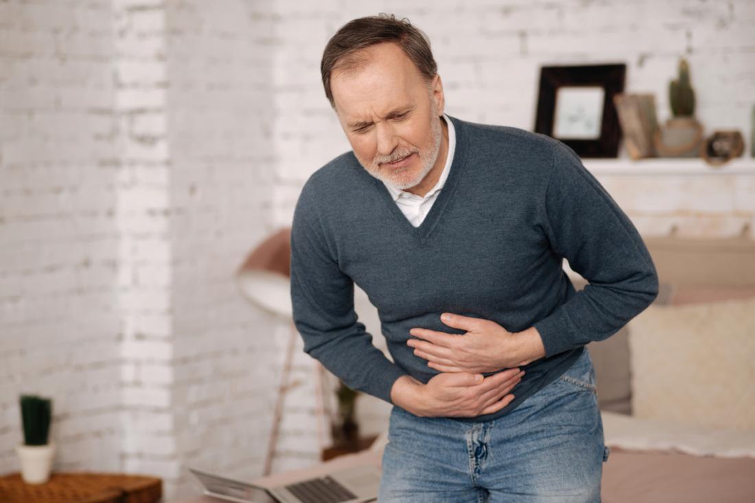 Man crouched over in pain, holding his stomach, suffering from IBS.