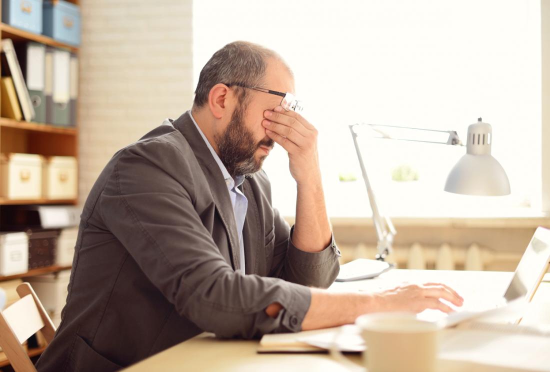 Man sitting at desk rubbing his eyes, stressed and with a headache.