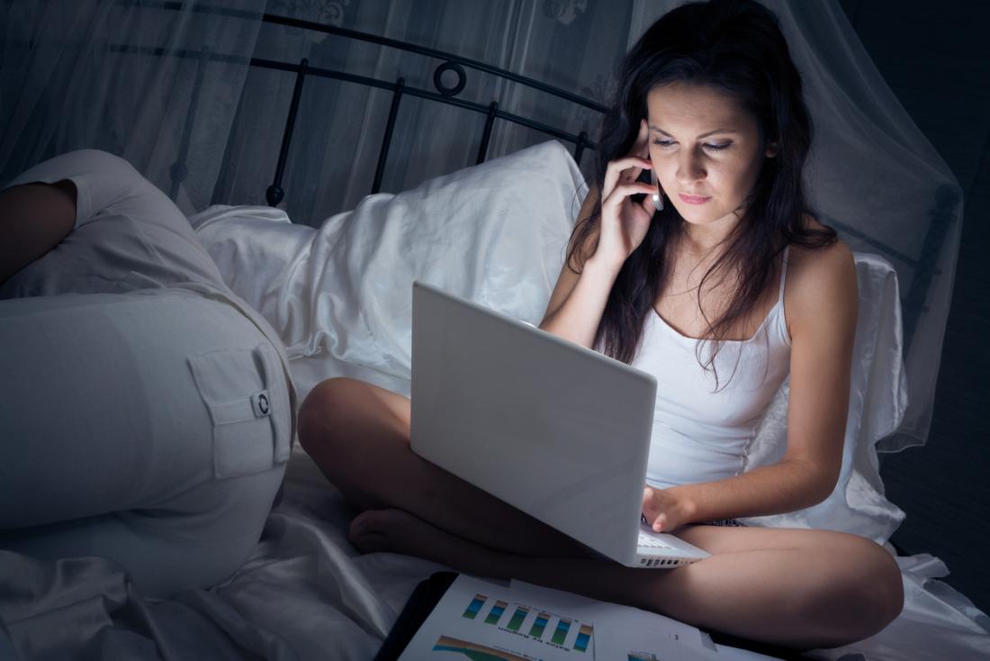 girl sitting on bed using phone and laptop