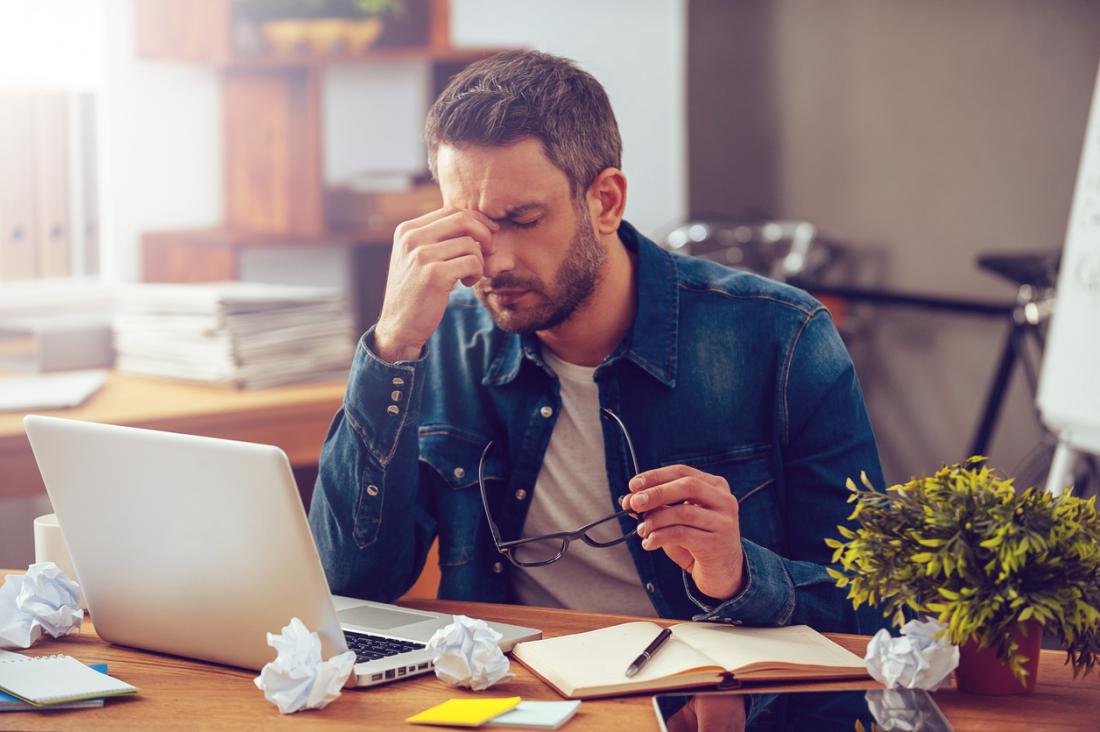 Stressed man at desk pinching the bridge of his nose because he has a headache.