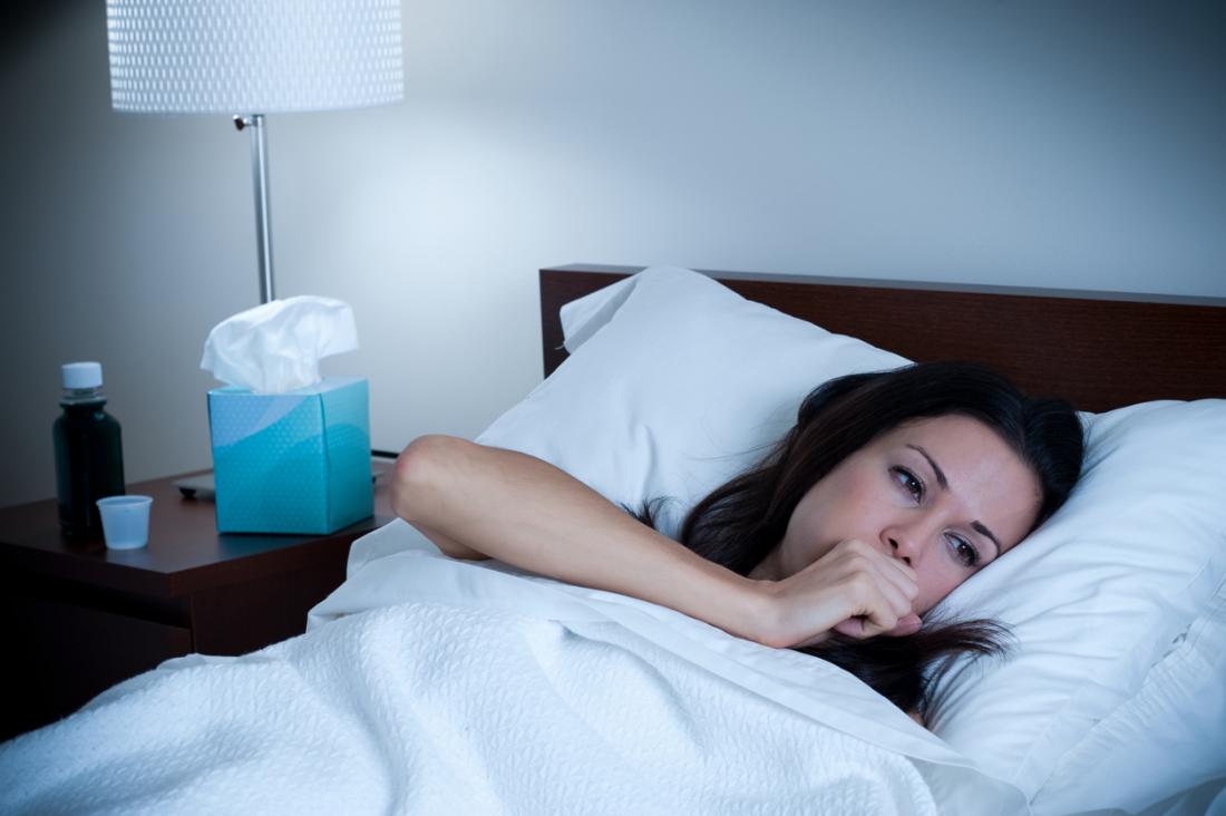 Woman coughing at night, with tissues and cough medicine by her bedside.