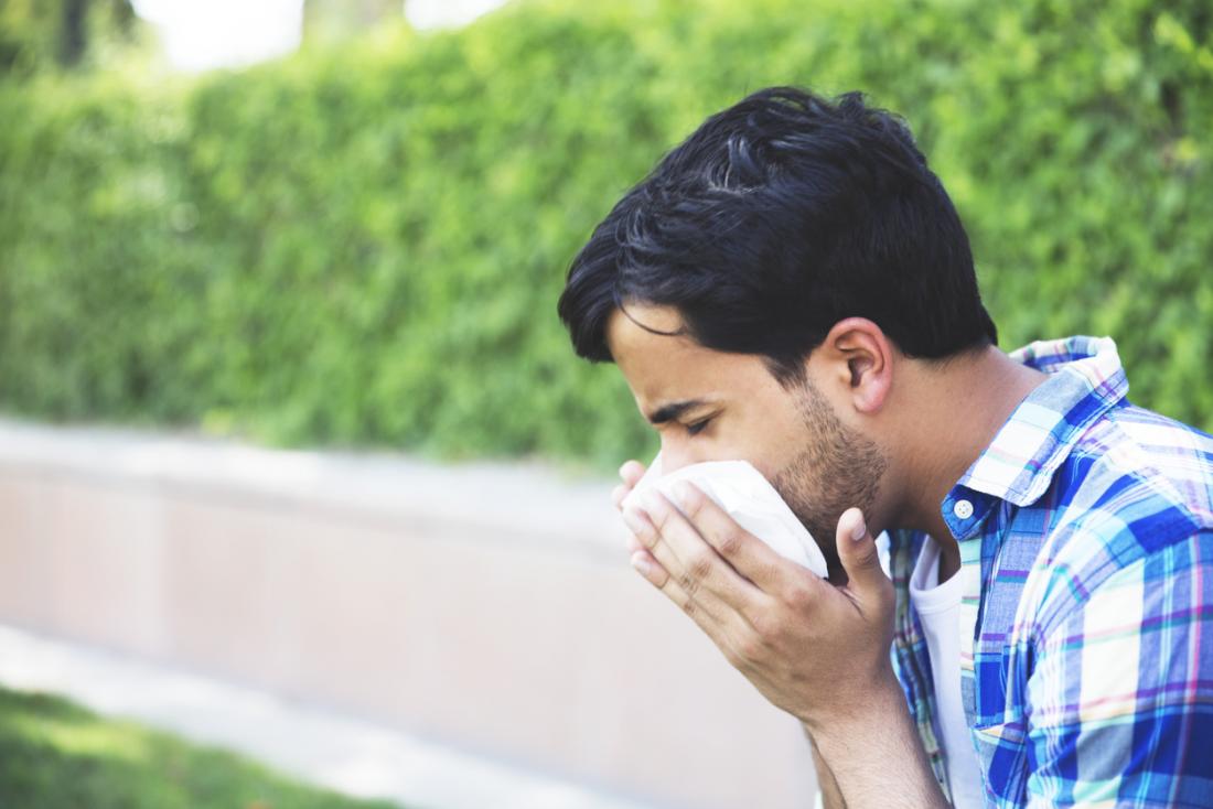 Man sitting outside in park, sneezing and blowing his nose.