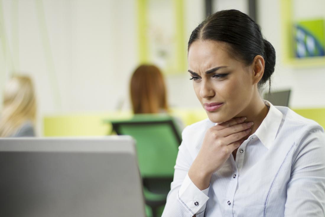 Woman at desk in office holding her throat with a pained expression.