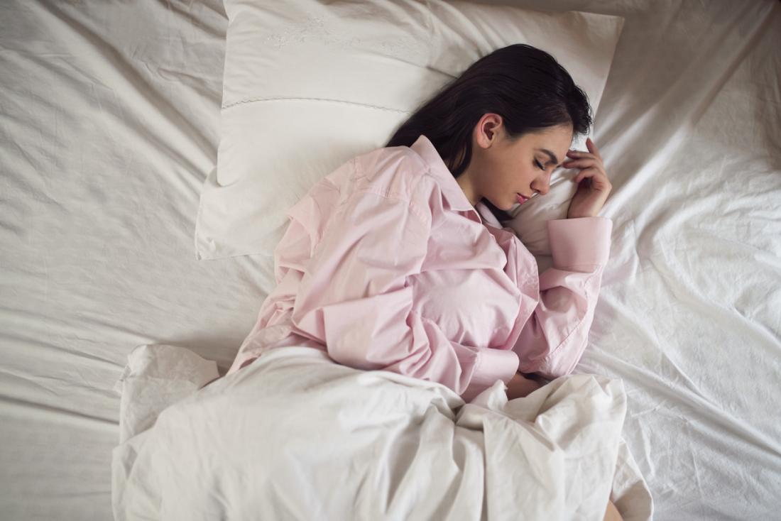 Woman in pyjamas sleeping on her side in bed.