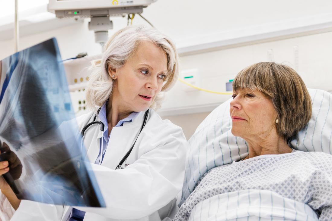 Mature female patient in hospital bed, with mature female doctor showing her an x-ray of her lungs.