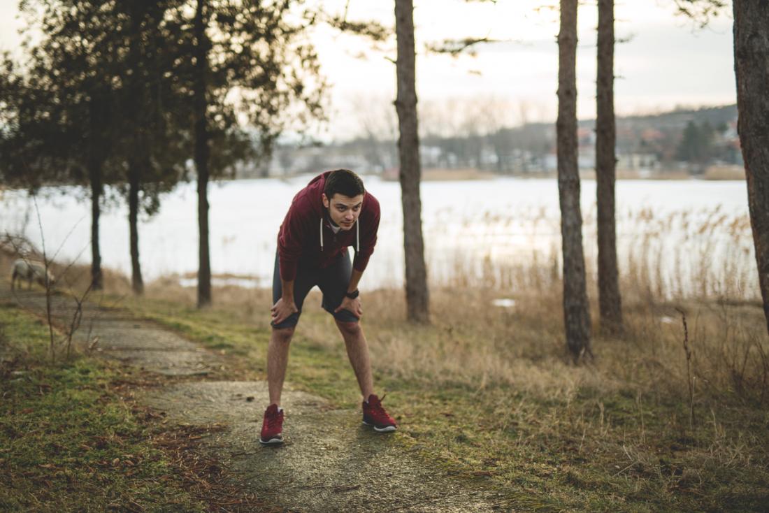 Young man in jogging gear, out of breath after running in woodland by the side of a lake.