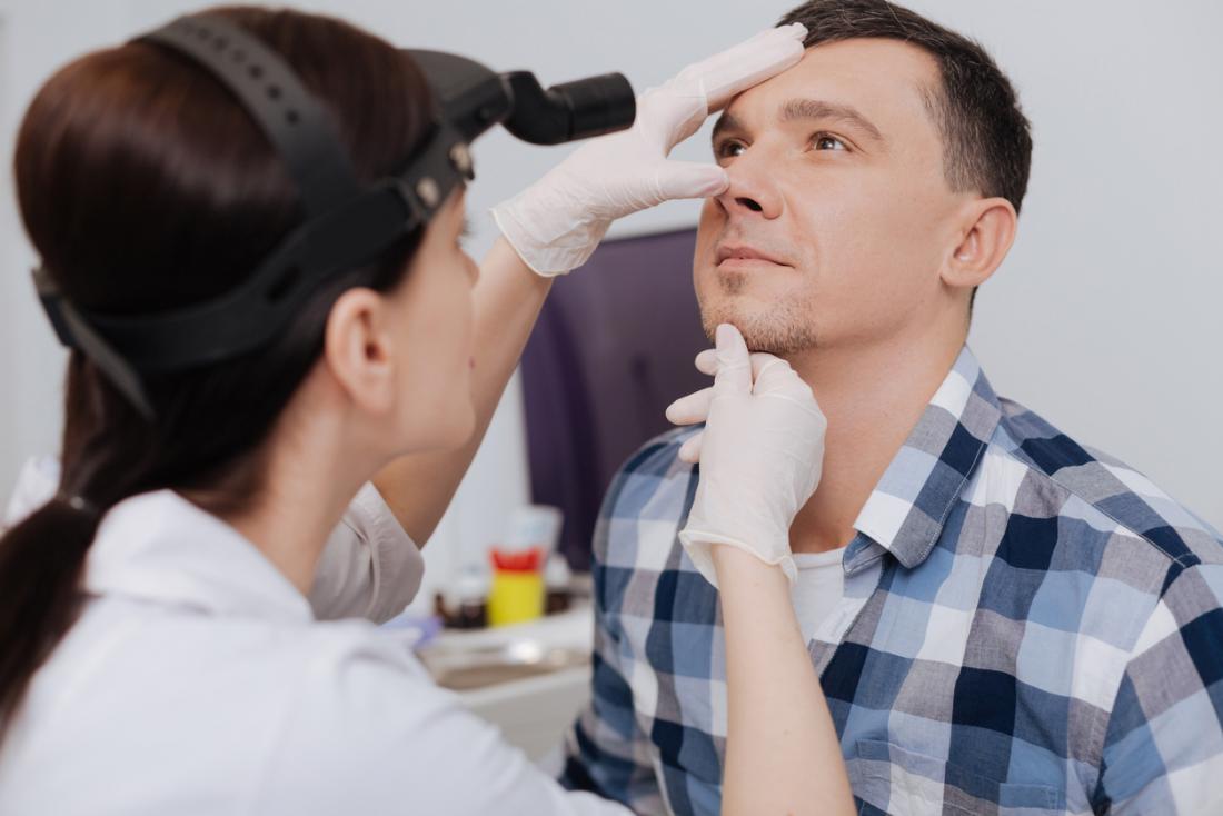 Female doctor inspecting male patient's nose.