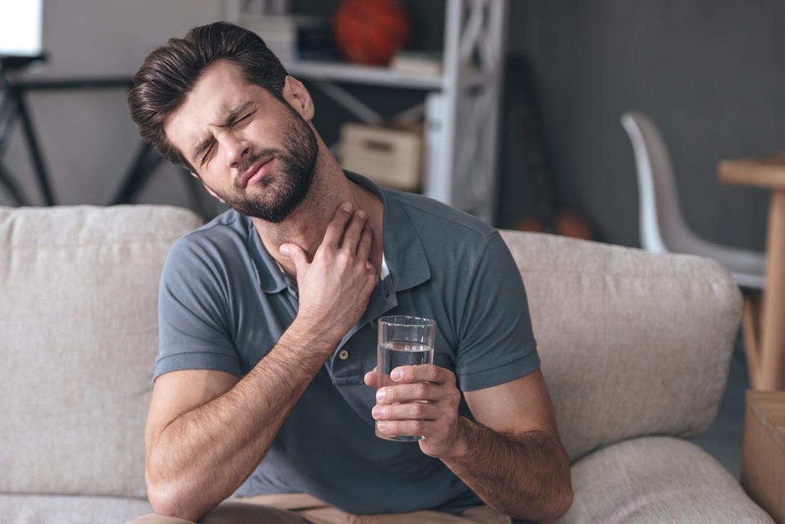 Man with painful sore throat, holding a glass of water.