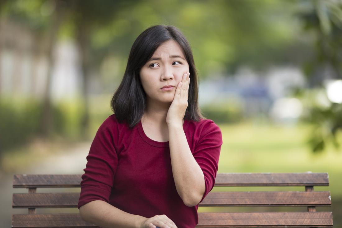 Woman sitting on a park bench holding her cheek in pain, because of a toothache or sore tongue.