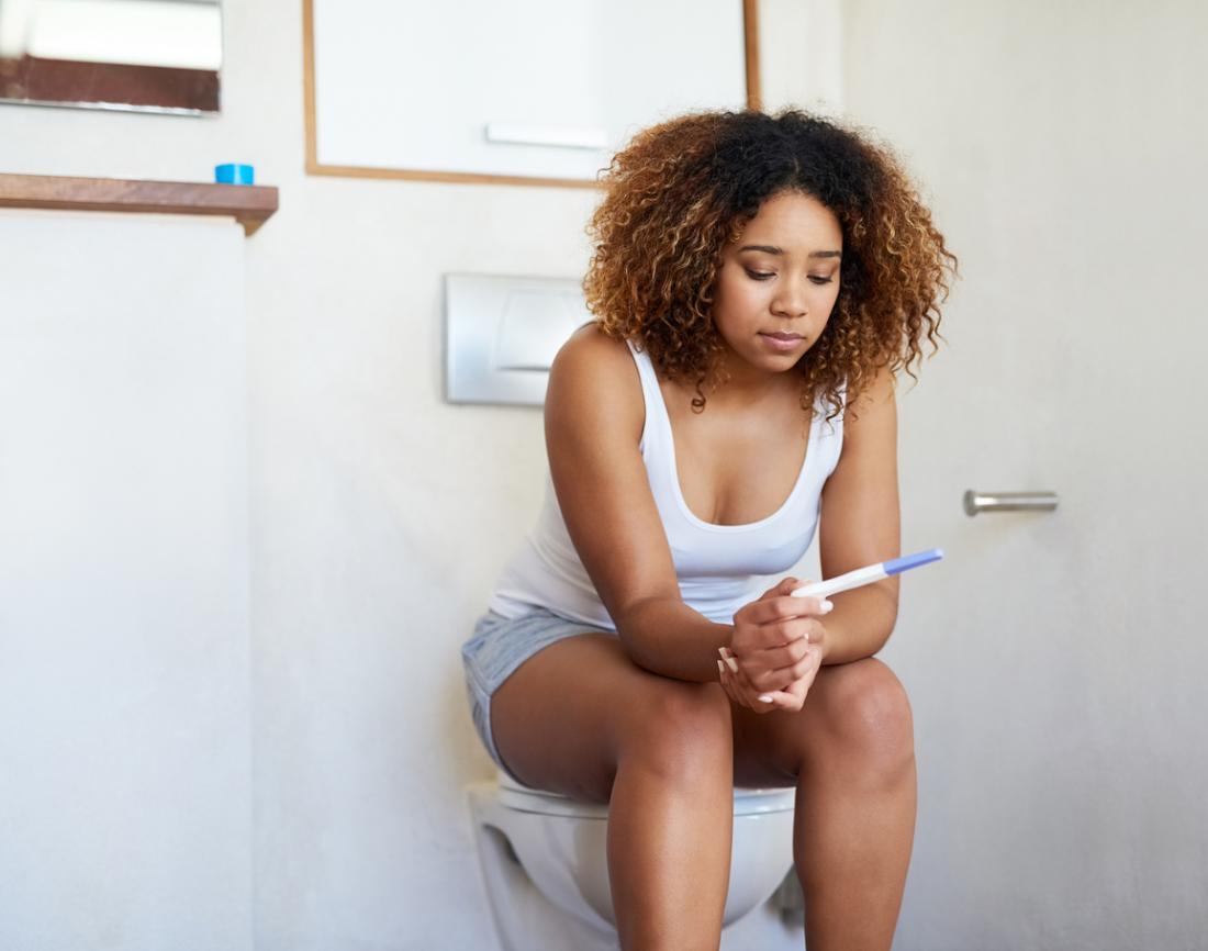Woman sitting on toilet looking at pregnancy test.