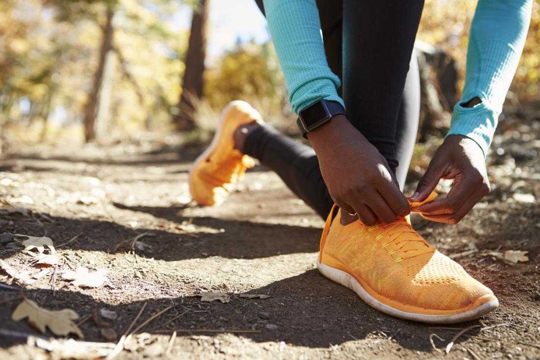 Woman tying shoelaces for running shoes/trainers, whilst outside in woods.