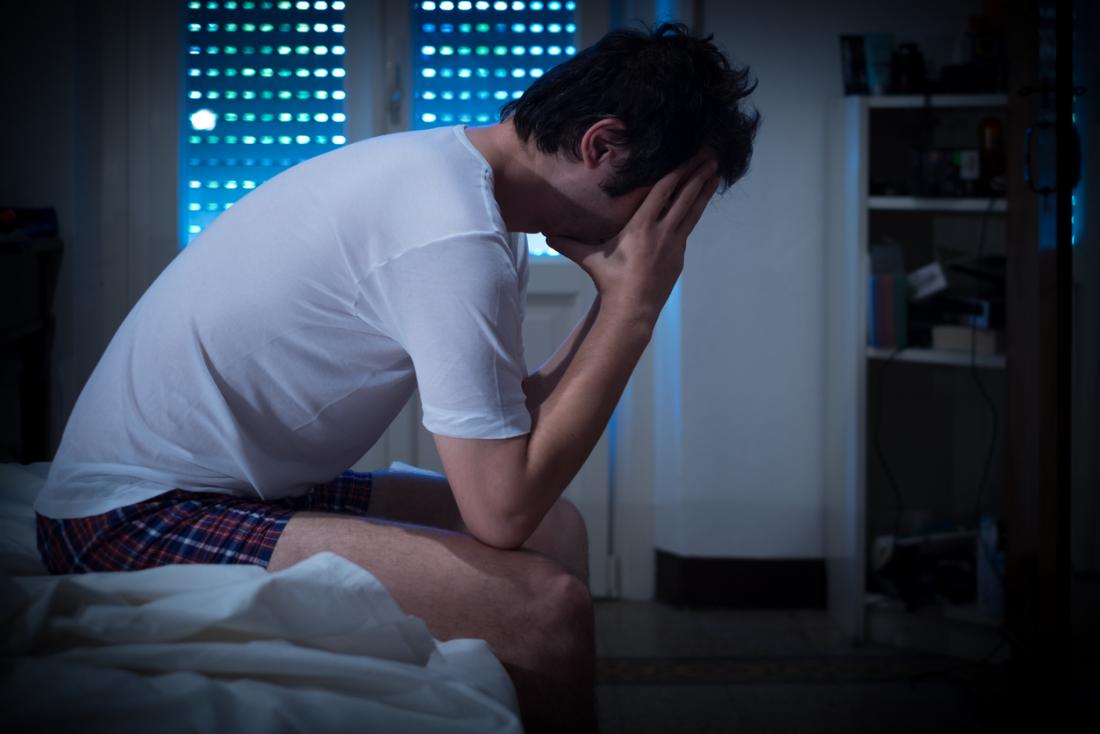 Man sitting o end of bed at night, unable to sleep because of insomnia.