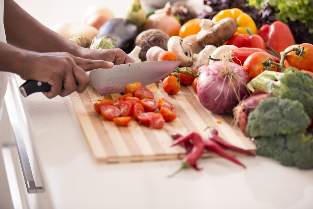 tomatoes being chopped up surrounded by other healthy vegetables