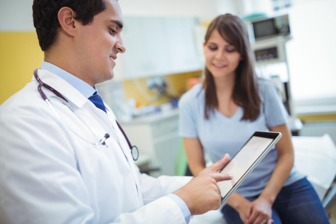 Male doctor speaking to young female patient while using tablet.