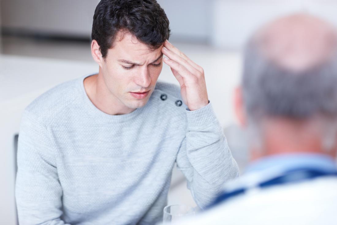 Man holding his head in pain, speaking to doctor about migraines.